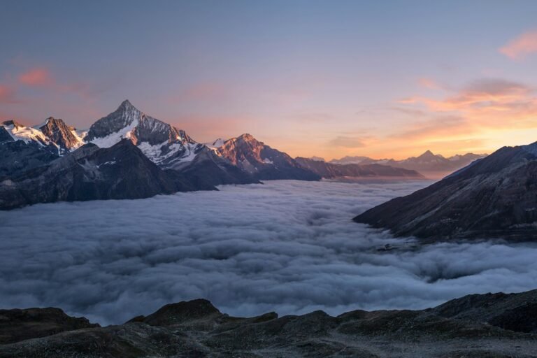 Snow-covered alpine peak rising above a cloud layer at sunrise