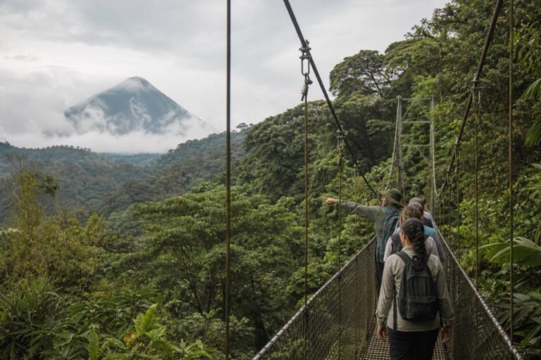 Small guided group walking across a suspension bridge above rainforest with Arenal Volcano beyond the canopy