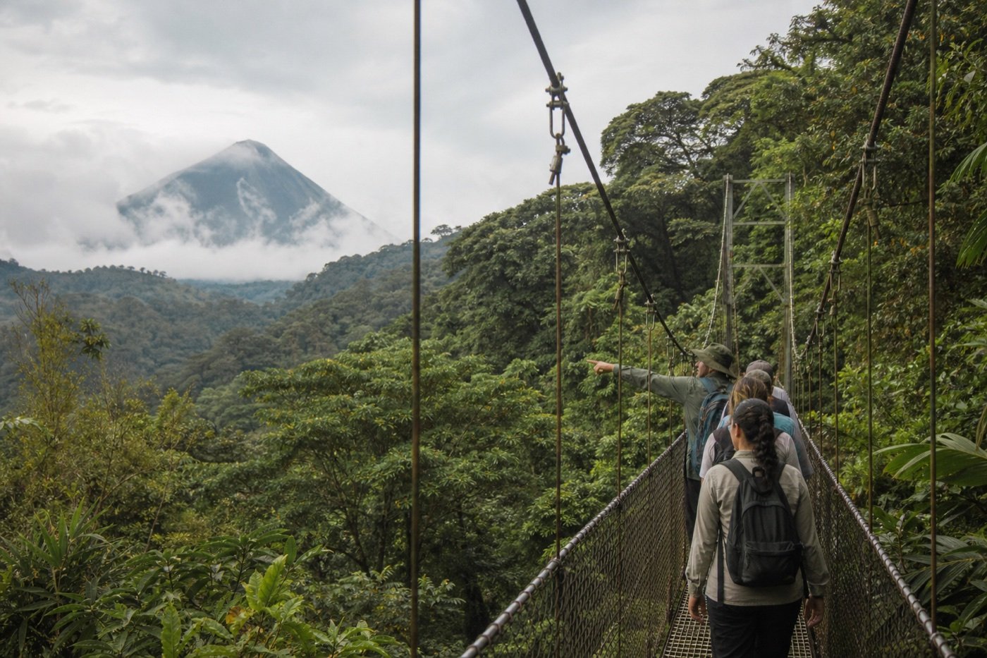 Small guided group walking across a suspension bridge above rainforest with Arenal Volcano beyond the canopy