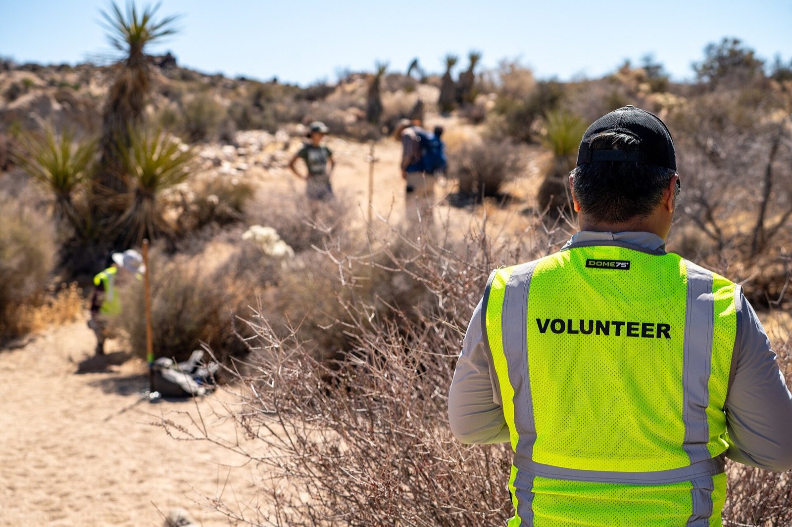 Conservation volunteers wearing safety gear while maintaining a desert hiking trail