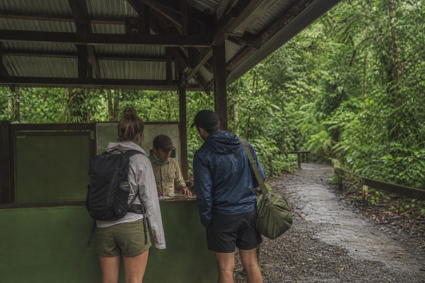 Two travelers with day and overnight luggage checking arrangements at a simple rainforest ranger station