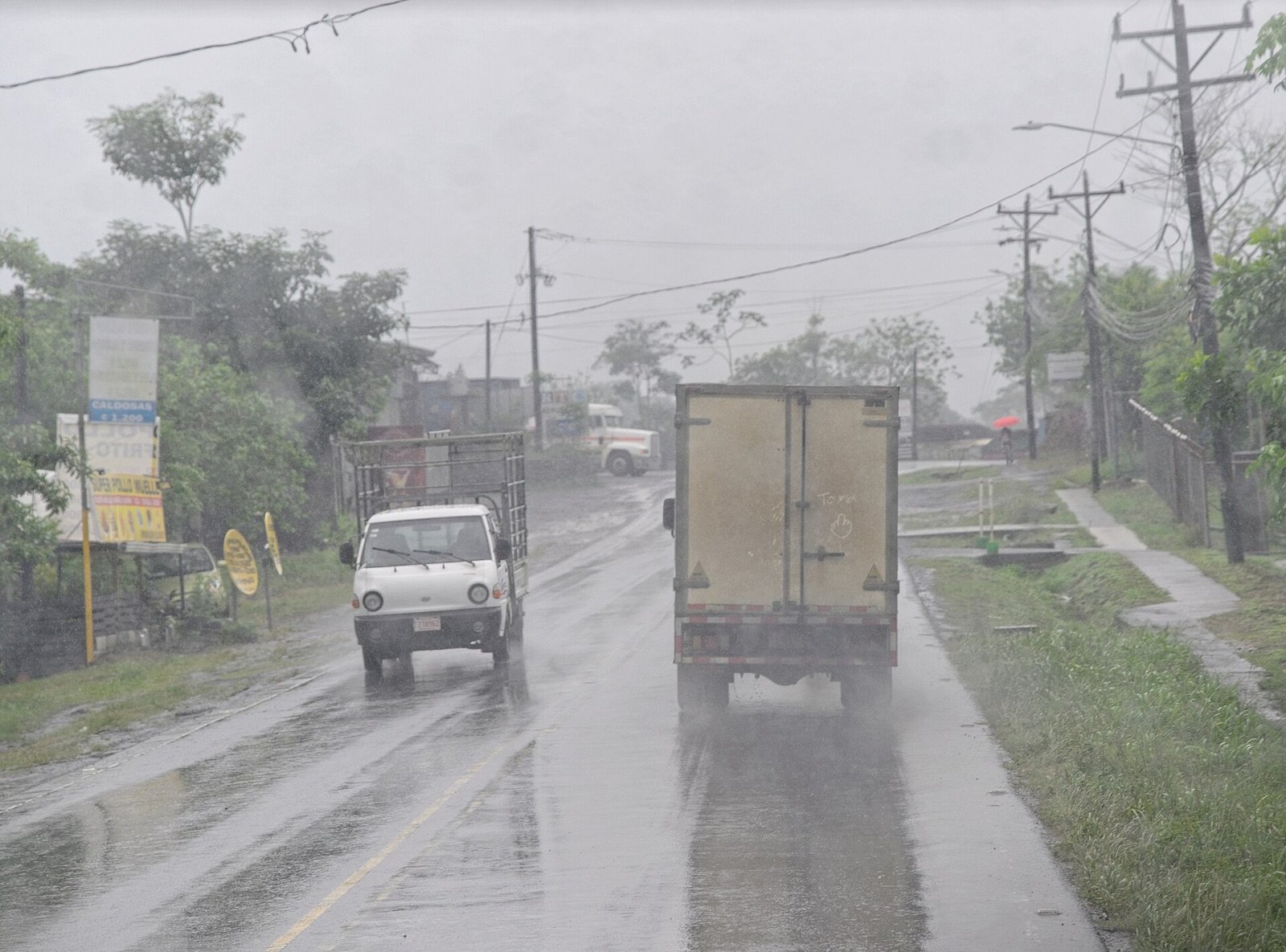 Cars and trucks traveling a wet two-lane road during heavy rain in Costa Rica