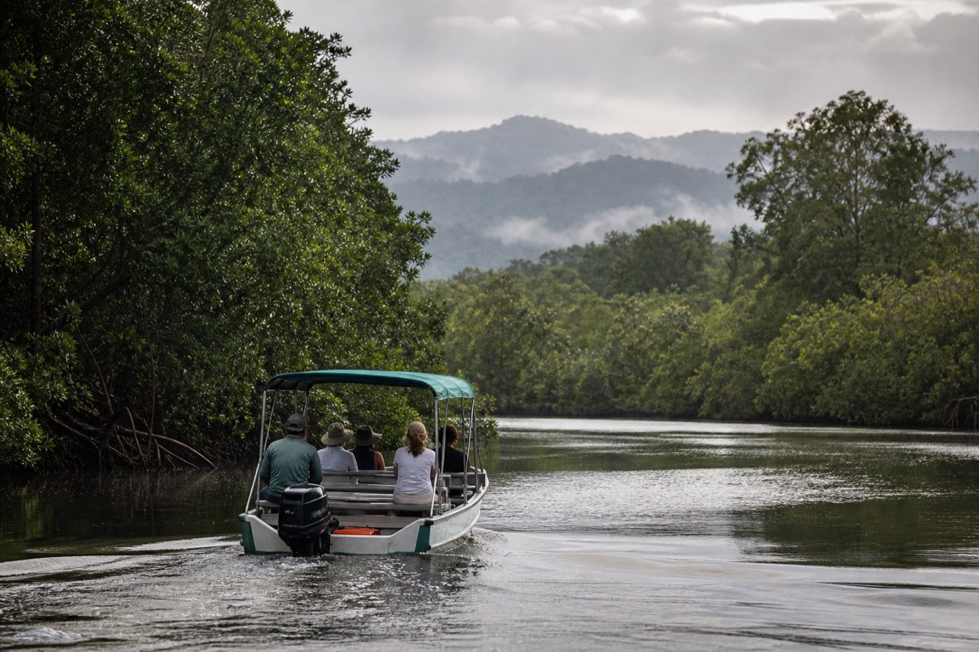 Small covered passenger boat moving slowly through a broad mangrove channel near Quepos