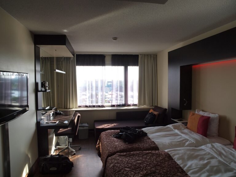 Modern hotel room with a bed, desk, chair, television, and wide window