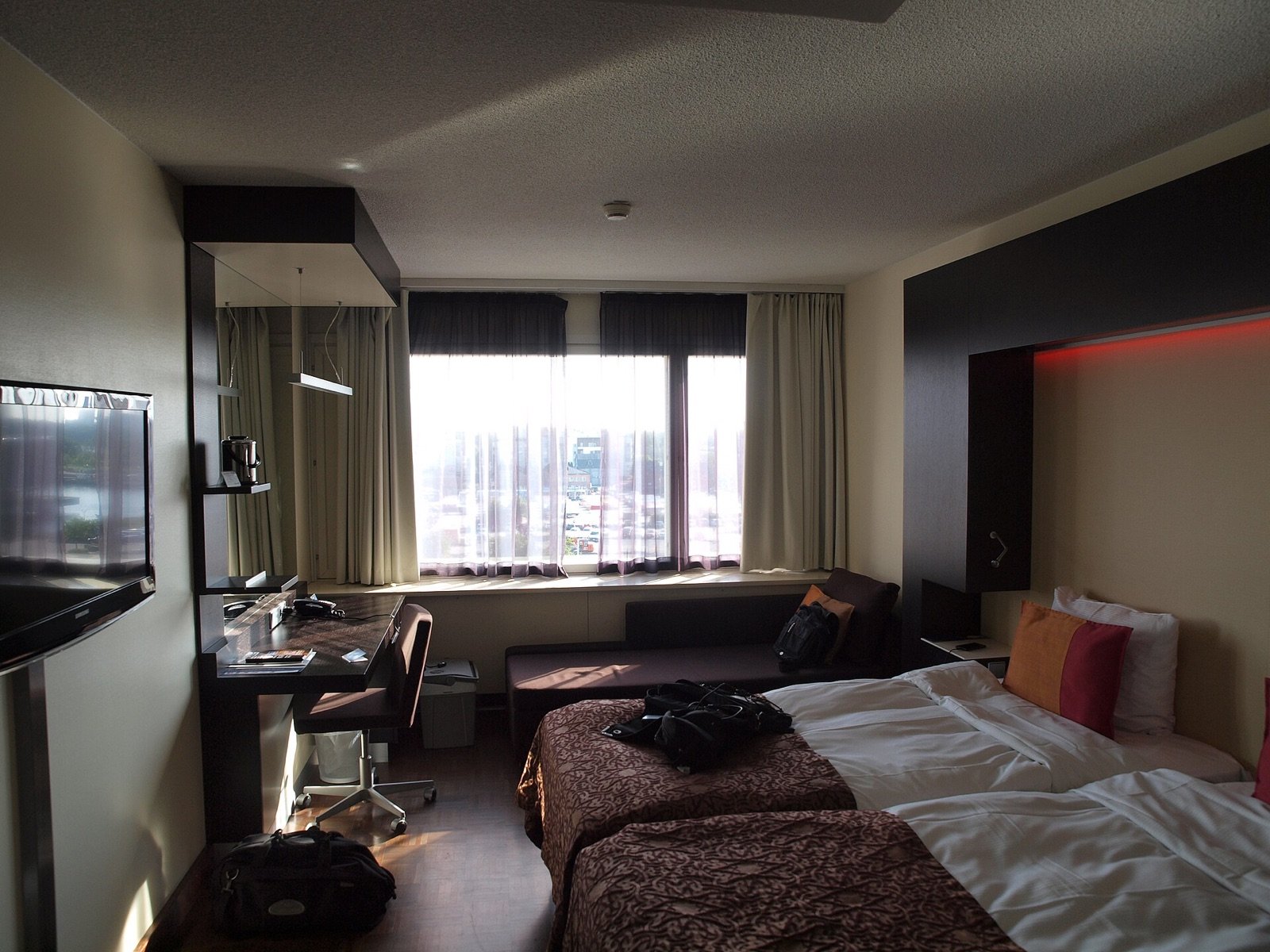 Modern hotel room with a bed, desk, chair, television, and wide window
