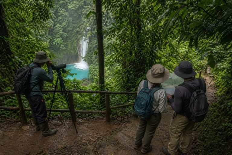 Guide with a spotting scope and two independent hikers consulting a map above the blue Río Celeste waterfall