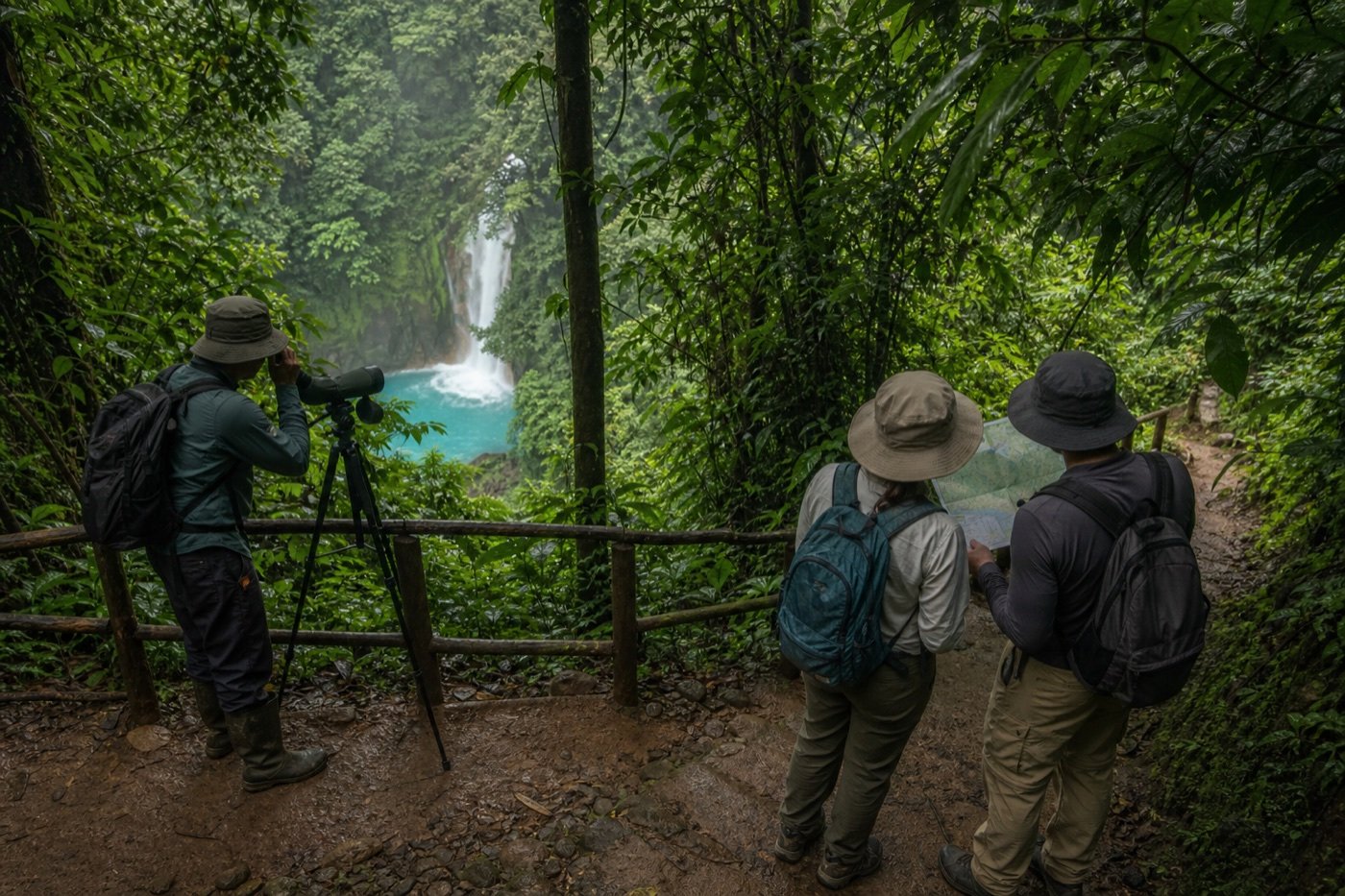 Guide with a spotting scope and two independent hikers consulting a map above the blue Río Celeste waterfall