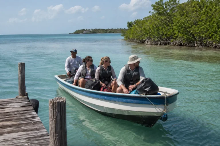 Travelers with compact soft luggage arriving by small passenger boat at a quiet mangrove caye dock in Belize