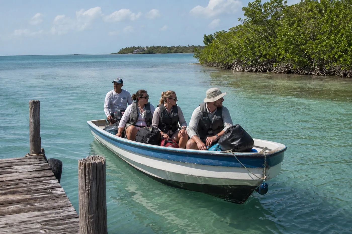 Travelers with compact soft luggage arriving by small passenger boat at a quiet mangrove caye dock in Belize