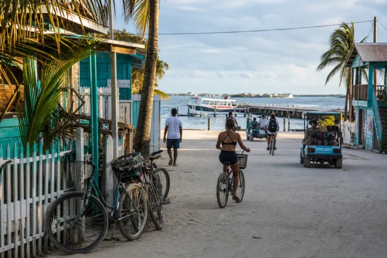 Bicycles on a sandy Caye Caulker lane leading toward a water taxi while golf carts move near the waterfront