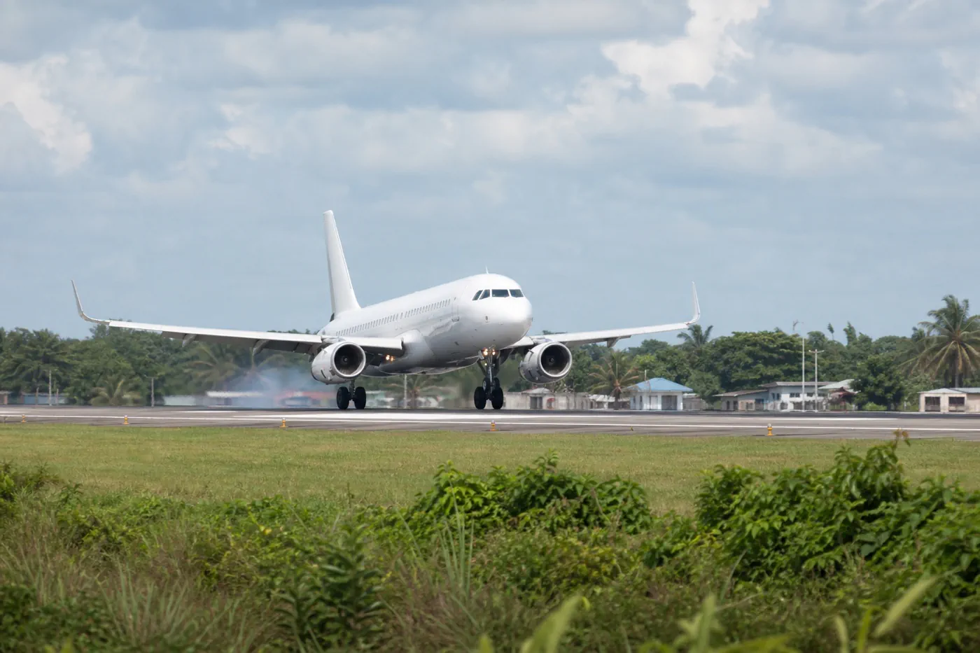 Unbranded passenger aircraft touching down on a tropical runway at Philip Goldson International Airport in Belize